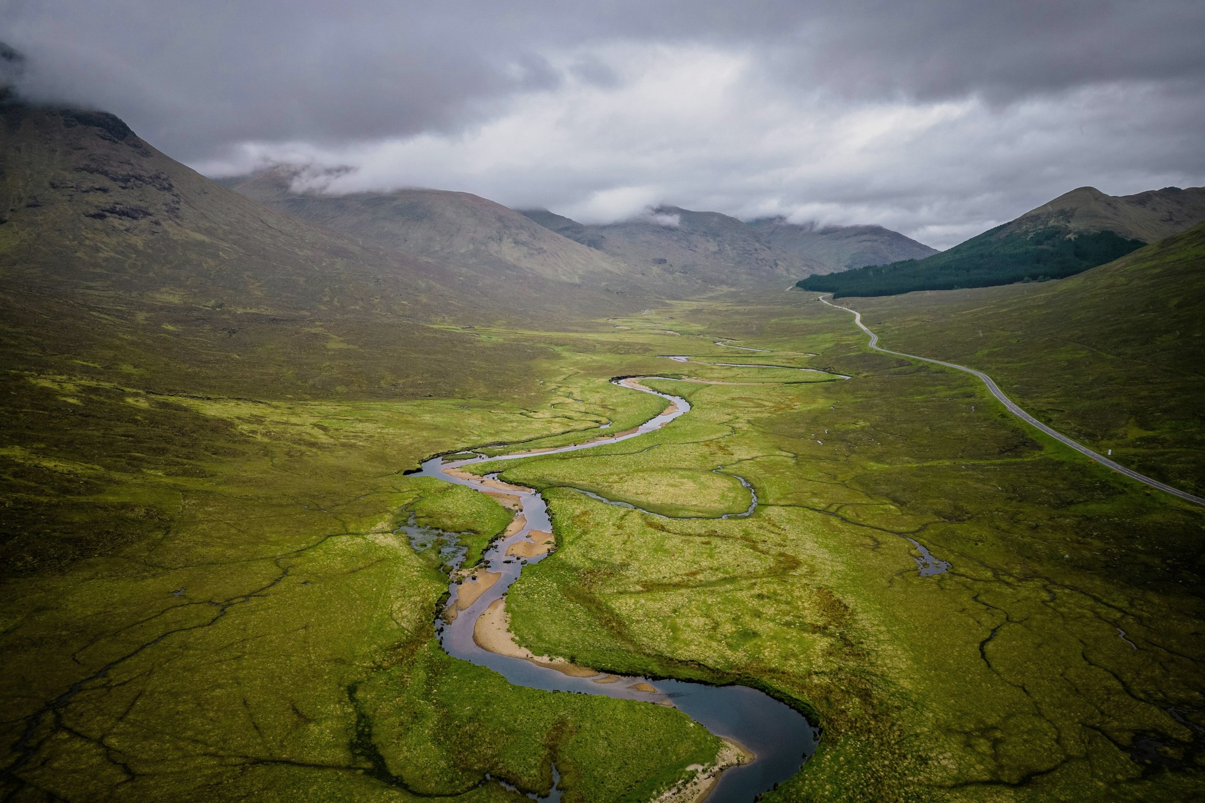 Aerial view of a river winding through a green valley under clouds
